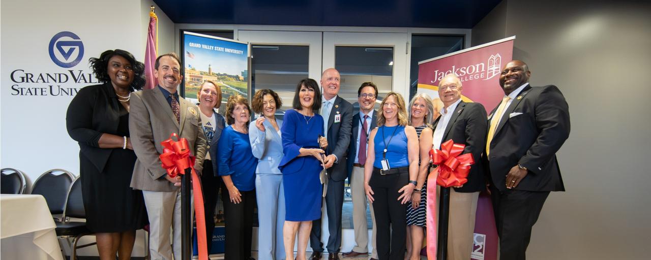 GVSU and Jackson College presidents and deans cutting red ribbon in front of GVSU office